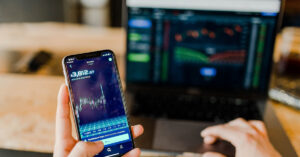 man looking at stock trends on his phone and laptop