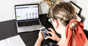 woman on her phone and laptop sitting at a desk