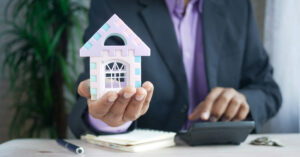 man in a suit holding a small model of a house