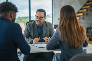 Business professional discussing a financial contract with two clients at a desk in a modern office, highlighting concepts of consultation, advice, and agreement