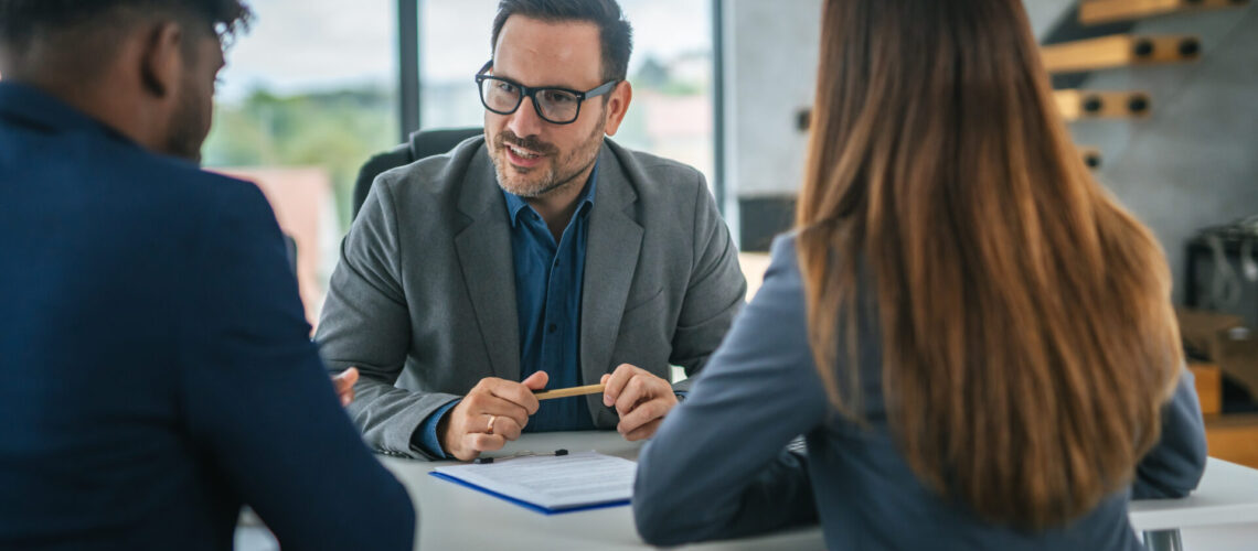 Business professional discussing a financial contract with two clients at a desk in a modern office, highlighting concepts of consultation, advice, and agreement