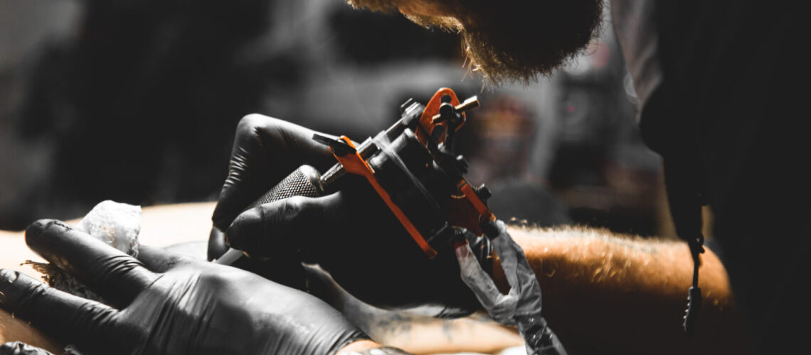 The tattoo artist creates a picture on the body of a man. close-up of tattoo machines and hands