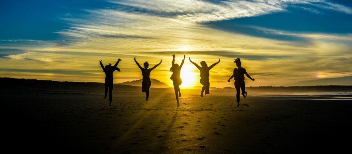 5 people jumping for a picture in front of a sunset